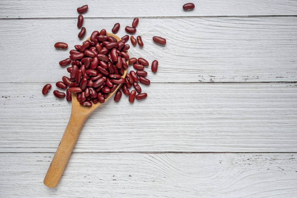 dried red beans or kidney beans in the wooden spoon on white wood background top view