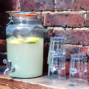 lemonade drink dispenser on shelf with glasses and plants