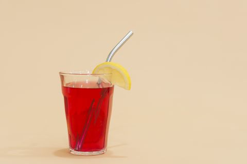 glass with reusable stainless steel straw and lemon in red drink