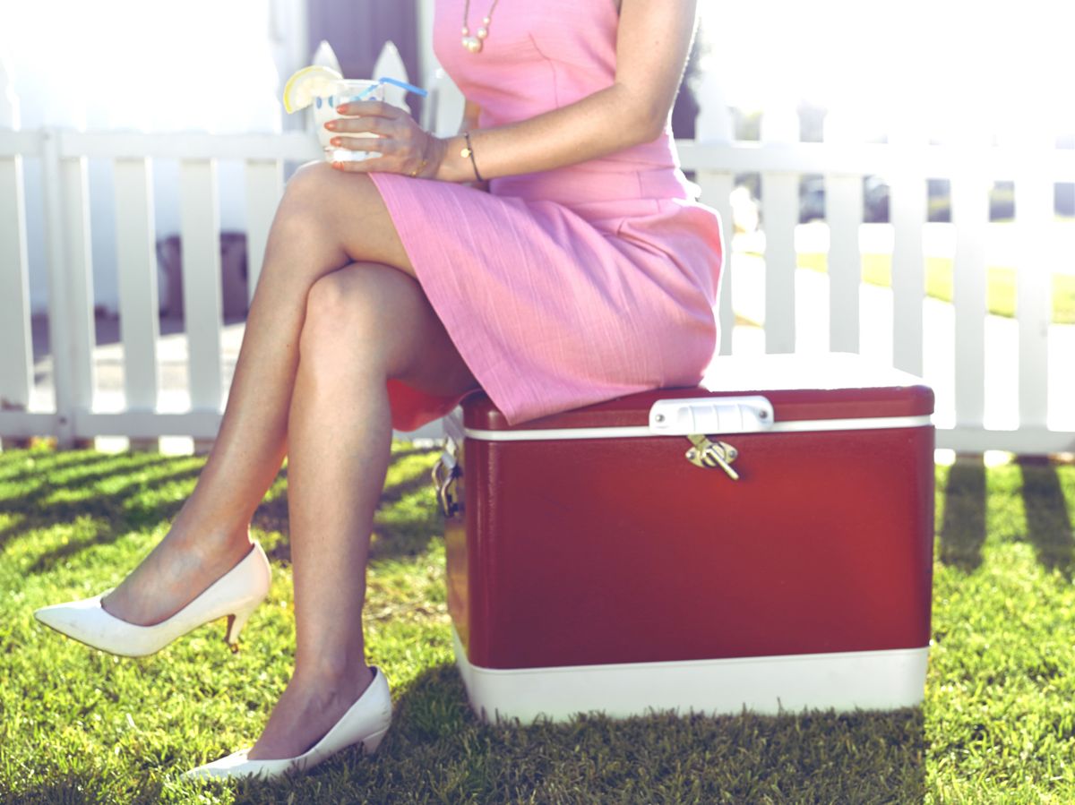 woman in a pink dress sitting on a red cooler
