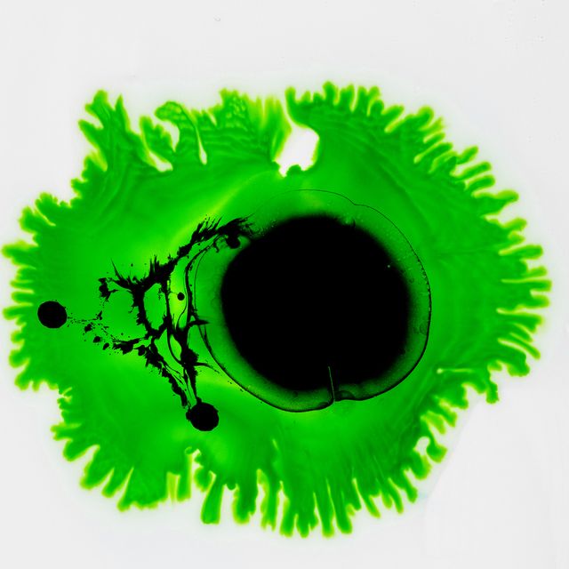 drop of black and green paint slides on a white canvas