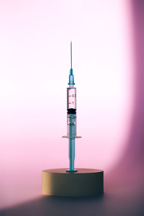 drop of clean transparent medication spilling from end of needle of disposable syringe against blue background with illuminating concept of fighting covid 19 front view and extreme close up