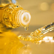 Argan Oil for Hair drops of bright yellow essential oil with air bubbles are dripping from glass bottle and pipette on ultimate gray surface trendy colors of the year 2021 extreme close up and front view
