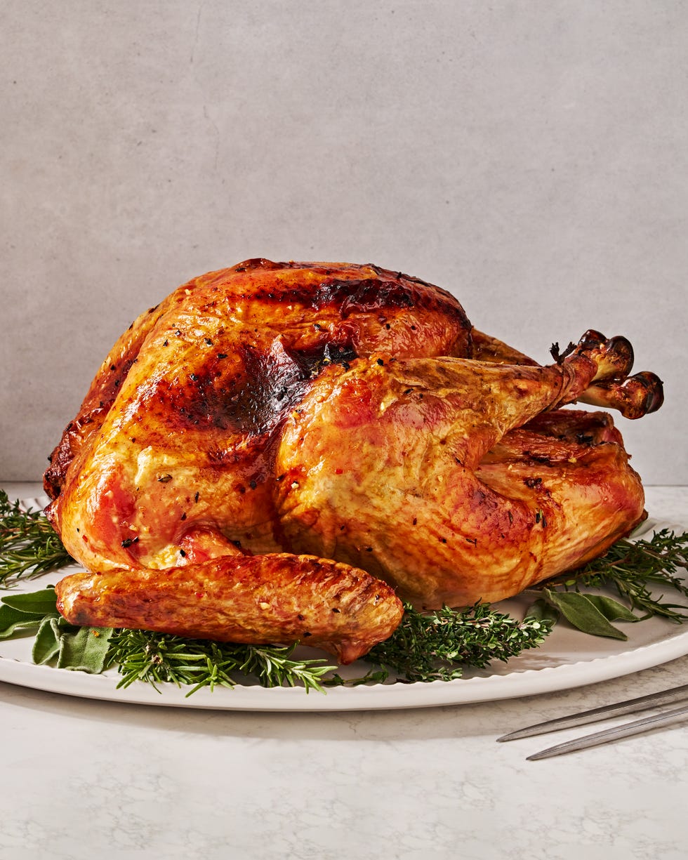 dry brine full turkey sitting on a white platter on top of fresh herbs