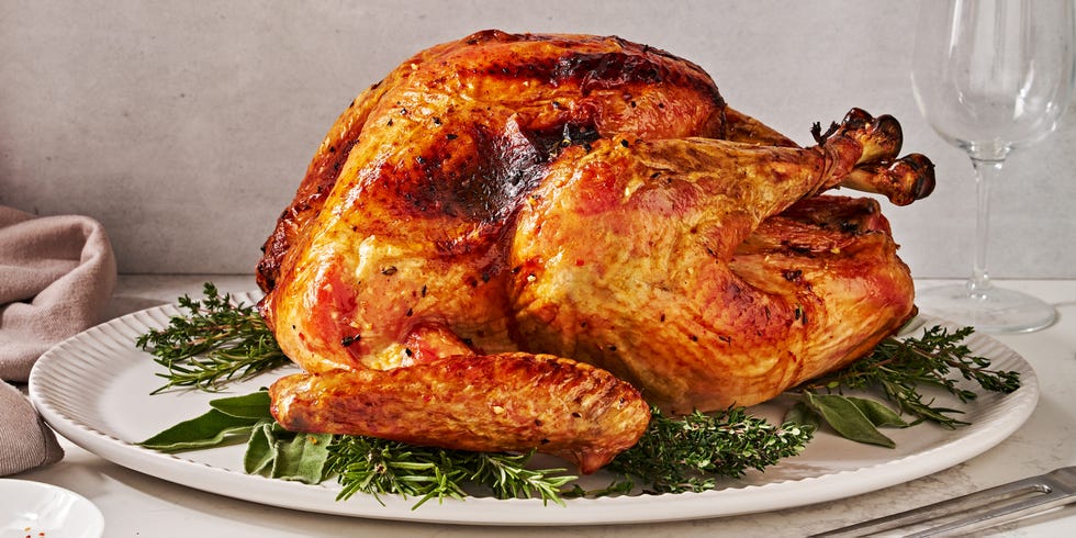 dry brine full turkey sitting on a white platter on top of fresh herbs