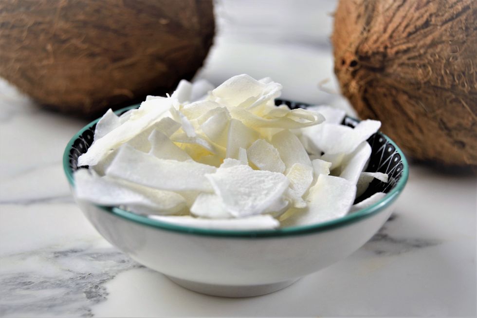 dry coconut flakes on a plate with coconuts on background