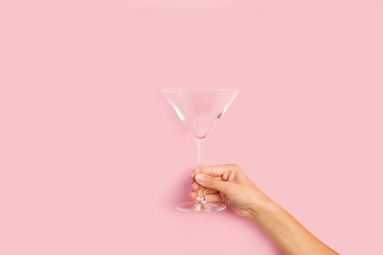 woman hand holding an empty cocktail glass on a pink background with copy space