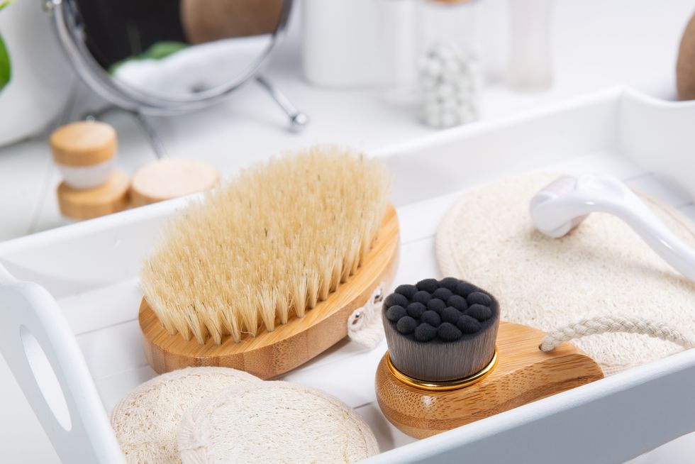 dry lymphatic drainage massage wooden brushes, derma mezoroller and loofah pads for face and body skin care on a white tray bathroom treatments homemade care natural beauty and zero waste concept