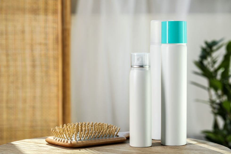 bottles of dry shampoos and hairbrush on wooden table