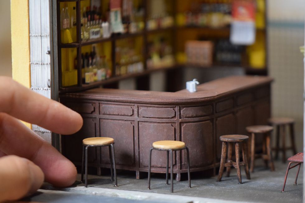 closeup of a miniature replica of a bar, with bar stools and a human hand for scale
