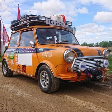 an orange mini hatch with a roof and decals rack sits on a dirt road