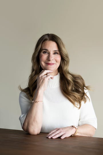a woman with long wavy hair seated at a table wearing a white sweater