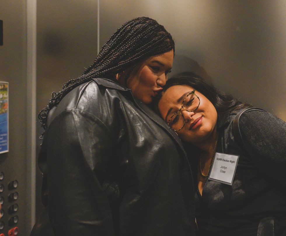two women in an elevator, one kissing the other on the head