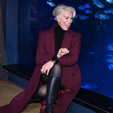 Hannah Waddingham came face to face with “Tiddler” and his aquatic friends, at Sea Life London Aquarium a person seated by a large aquarium featuring various fish and a ray