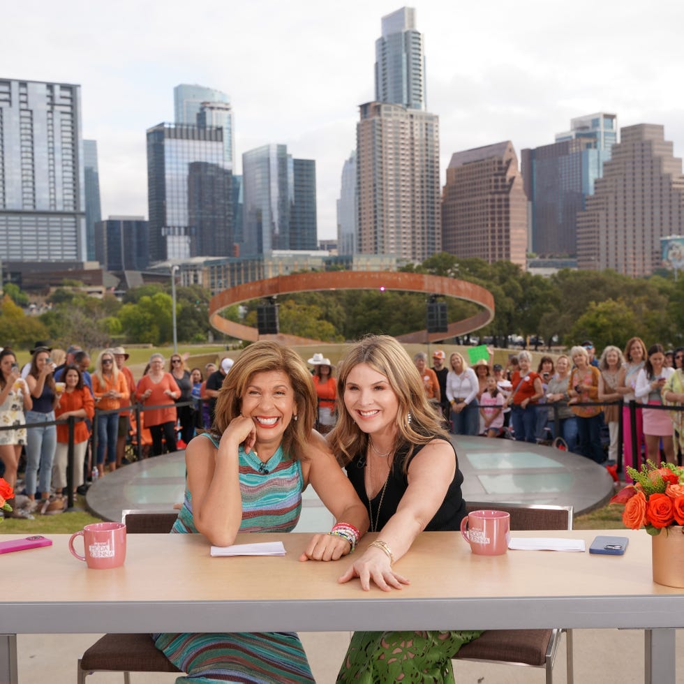 two women interact at a table with a city skyline in the background