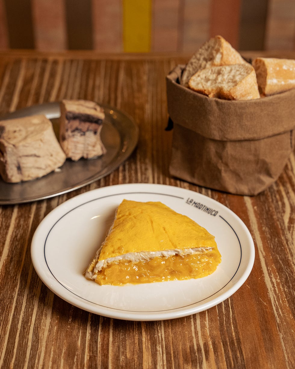 yellow dessert slice on a plate with bread and pastries in the background