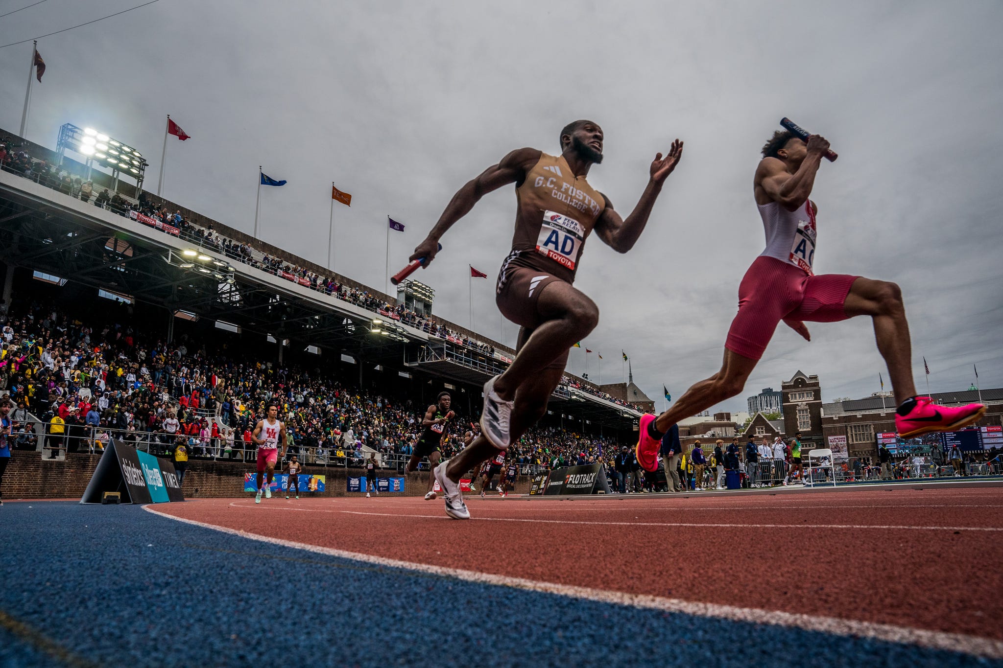RWD two runners sprint with a crowd behind them in a large grandstand