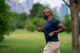 A person jogging in a green park setting with a city skyline in the background