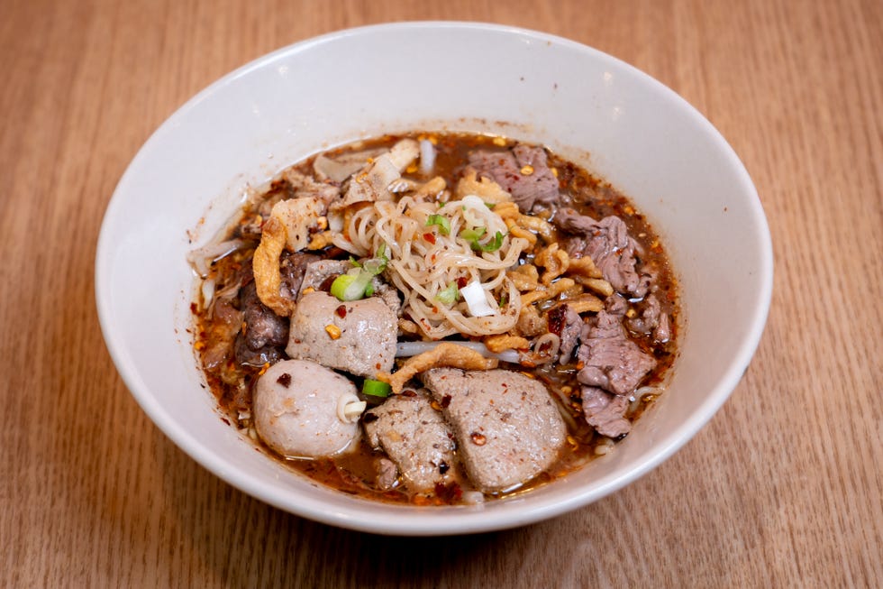 bowl of noodle soup with various meats garnished with herbs and spices