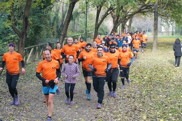 a group of runners wearing orange shirts jogging along a leafcovered path in a wooded area