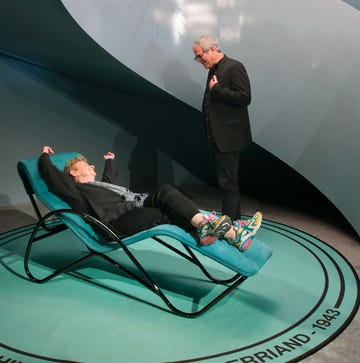 a person standing on a person lying on a chair in a room with lights