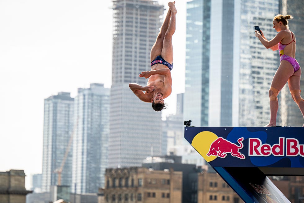 aidan heslop of the uk dives from the 27 metre platform while molly carlson of canada films from the lower platform during the second competition day of the sixth stop of the red bull cliff diving world series in montreal, canada on august 24, 2024