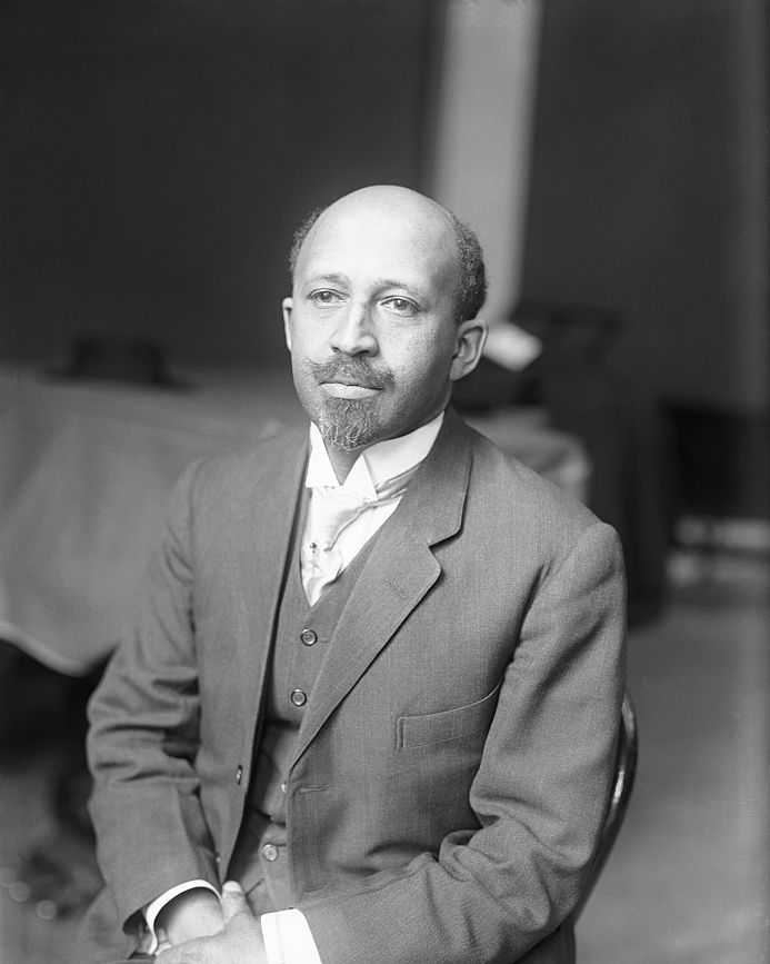 web dubois sits in a chair and wears a three piece suit with a tie