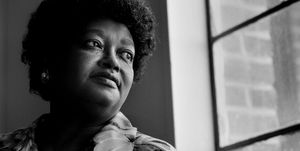 claudette colvin looks out a window, she wears a floral patterned collared shirt and an earring