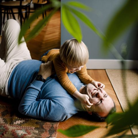 playful daughter pinching cheerful father's cheeks on floor at home