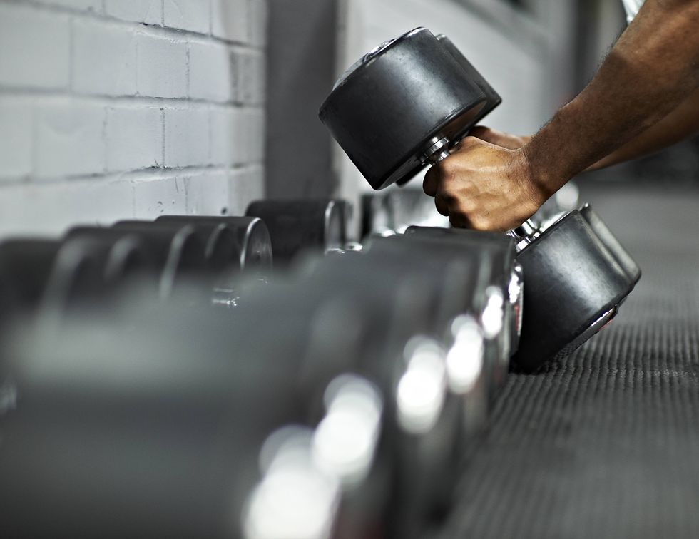 strong black male picking up dumbbells from selection of free weights in gym, ready for workout