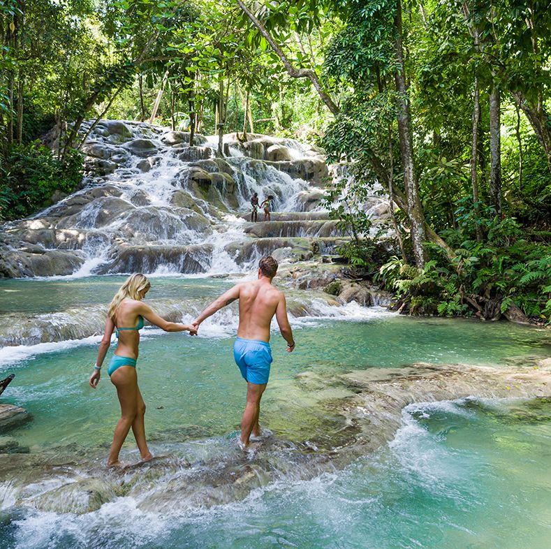 a man and woman walking by dunn’s river falls