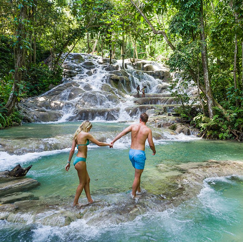 a man and woman walking by dunn’s river falls