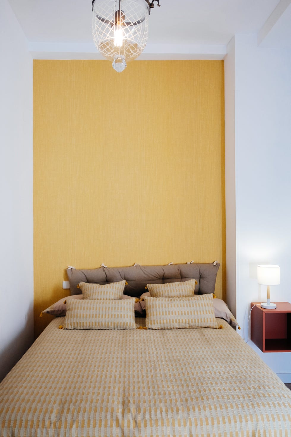 dormitorio con cabecero acolchado marrón y pared del cabecero con papel pintado amarillo