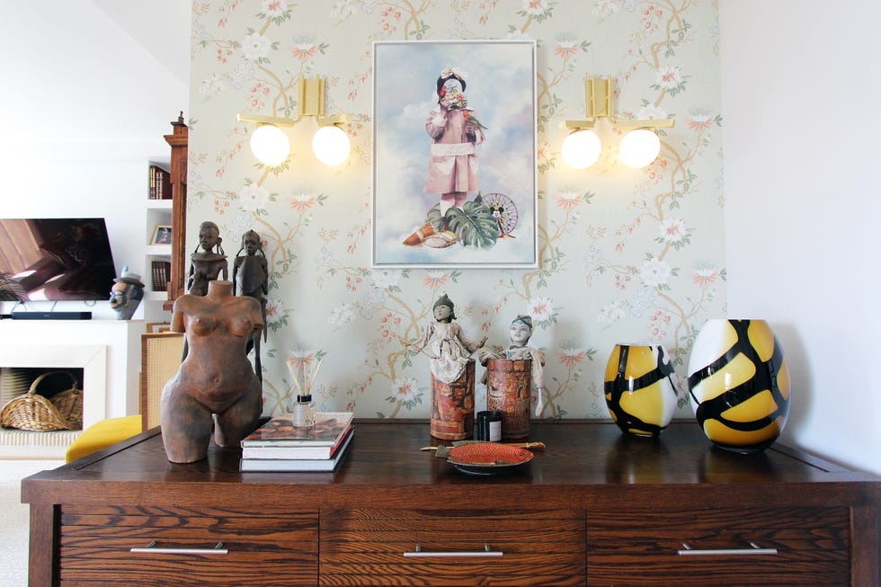 aparador decorado con piezas de arte y pared con papel pintado floral y apliques dorados