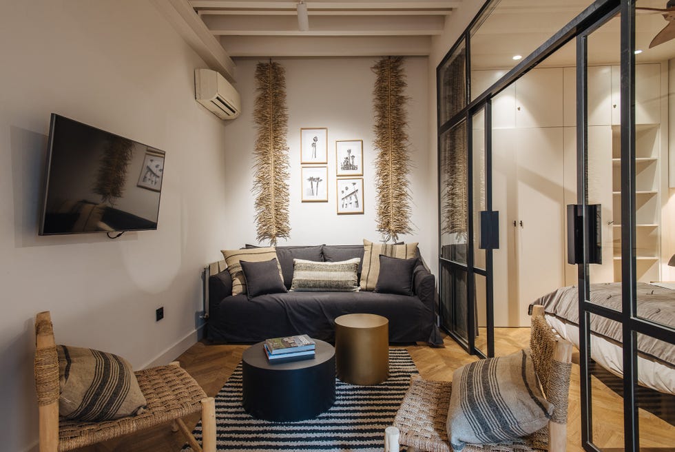 salón decorado en madera y fibras naturales junto a un dormitorio con cerramiento de vidrio con perfilería metálica