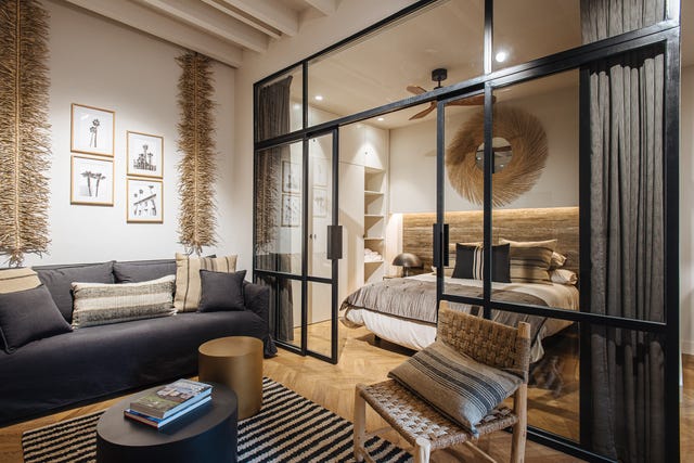 salón decorado en madera y fibras naturales junto a un dormitorio con cerramiento de vidrio con perfilería metálica