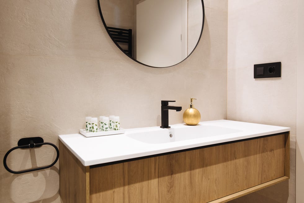 mueble moderno bajo lavabo de madera sin tiradores, grifería negra y espejo redondo con marco metálico negro