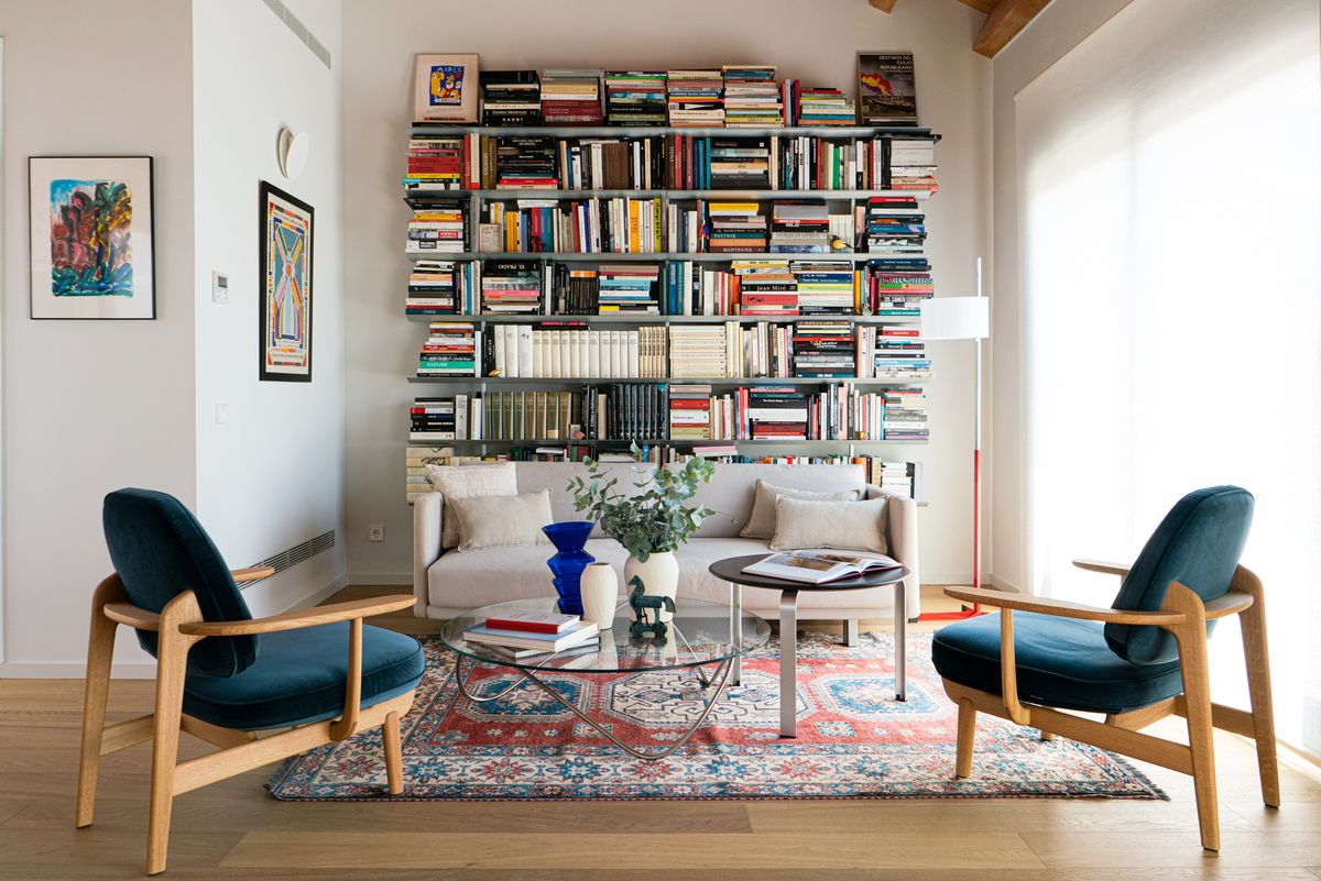 salón con sofá gris, dos butacas tapizadas en azul y librería de diseño moderno abierta