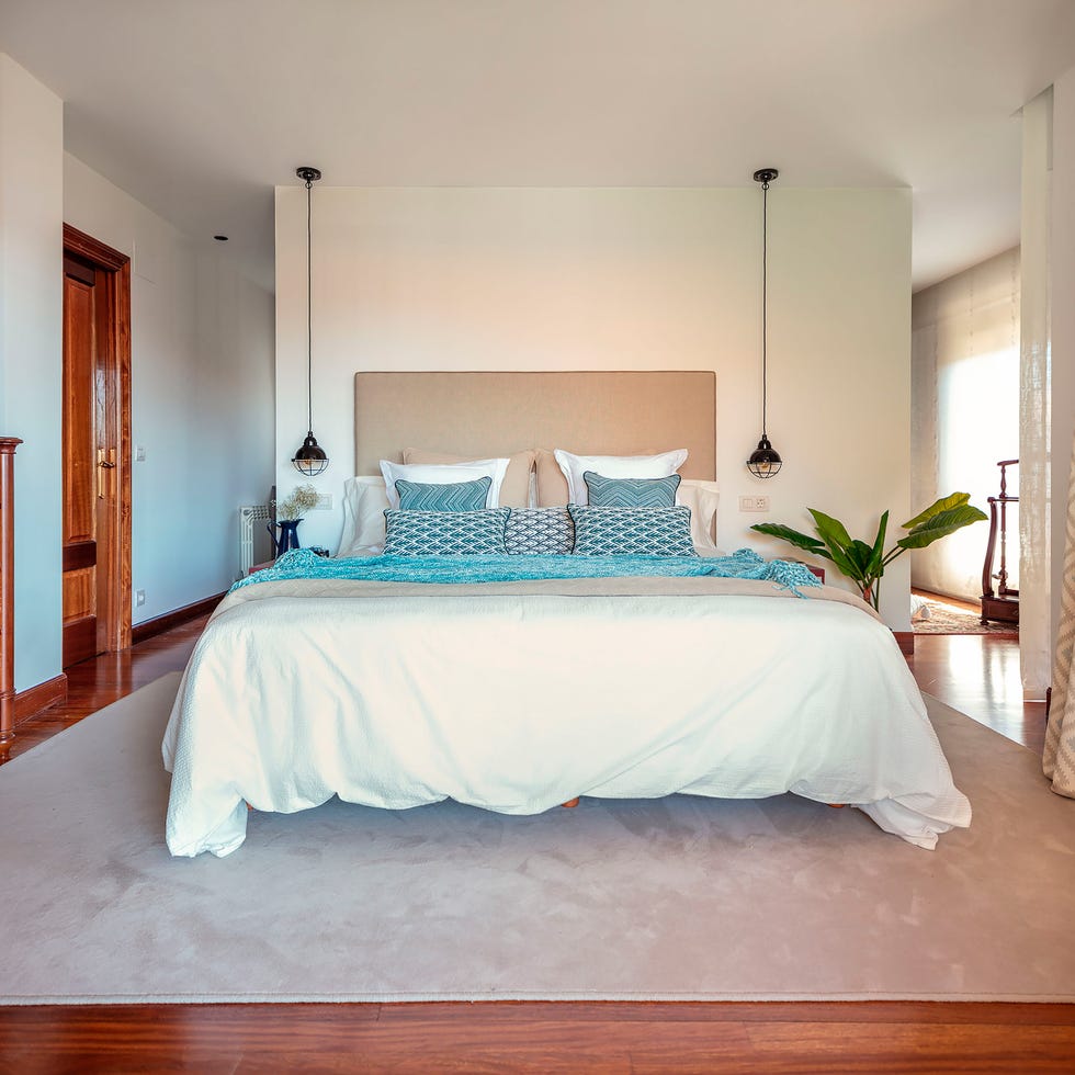cama con cabecero de color visón y lámparas colgantes industriales