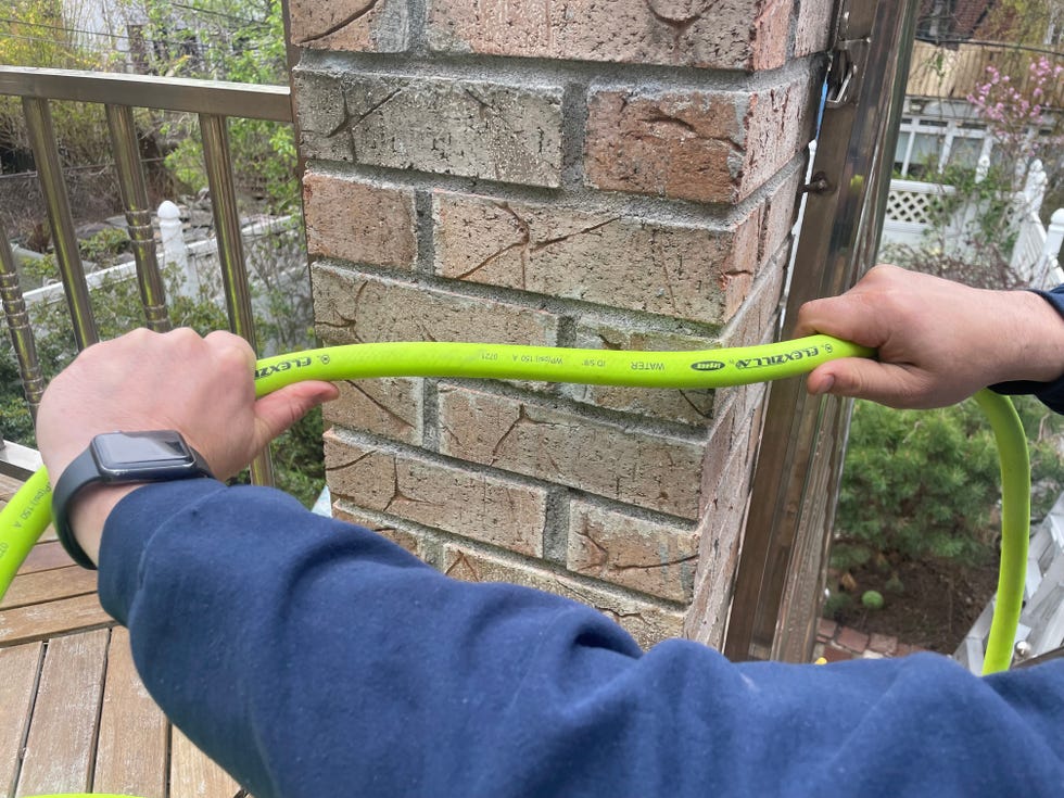 a product tester drags a green garden house across a brick pier