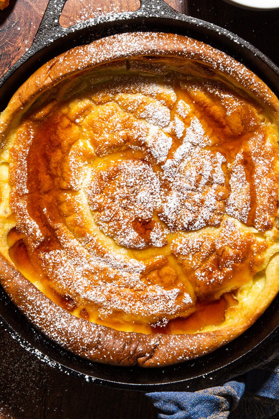 dutch baby pancake in a black cast iron skillet topped with maple syrup and powdered sugar