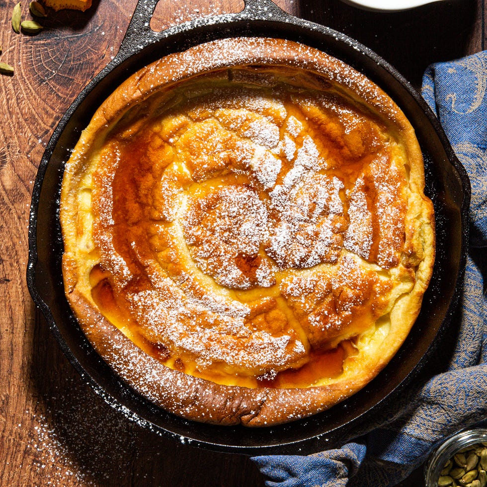 dutch baby pancake in a black cast iron skillet topped with maple syrup and powdered sugar