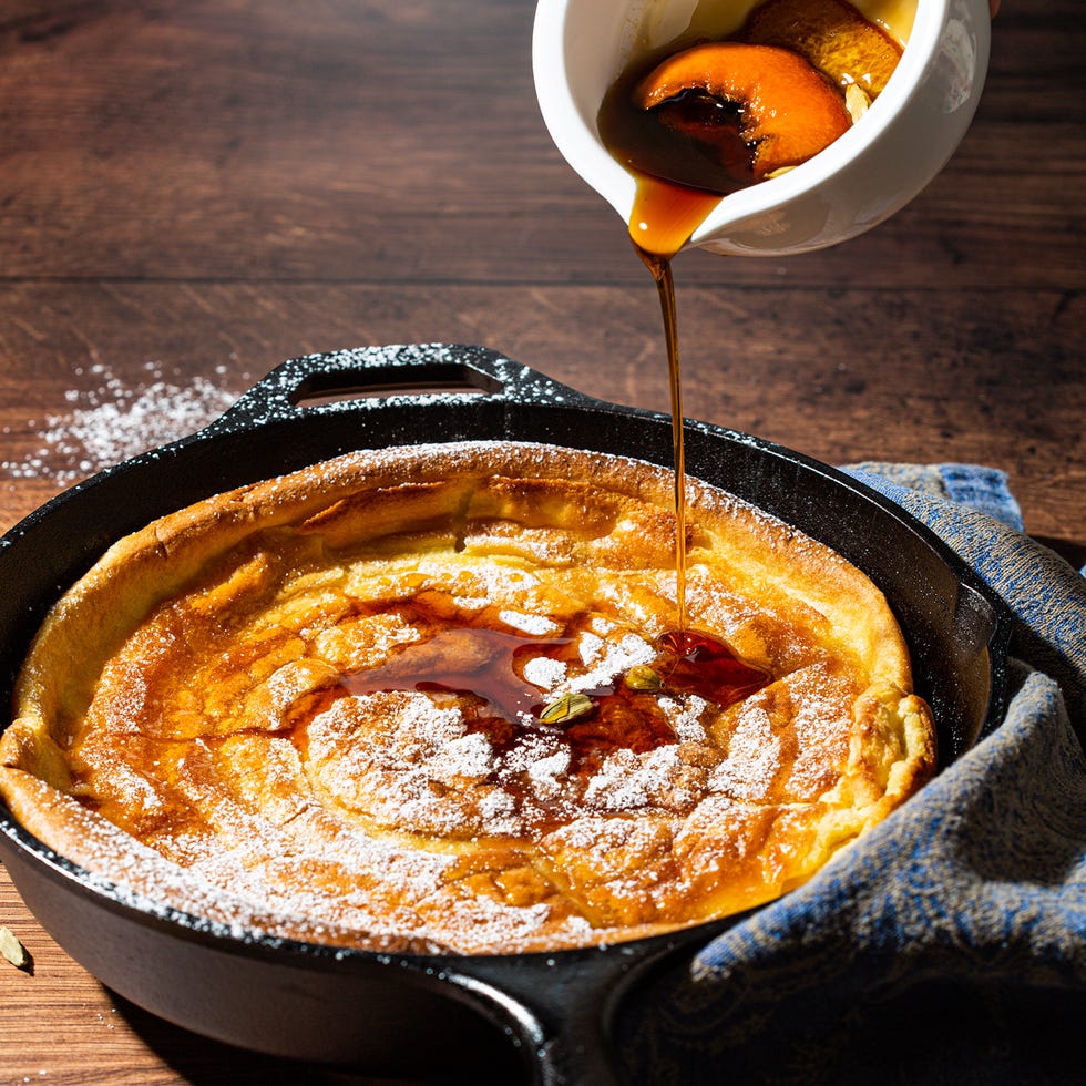 dutch baby pancake in a black cast iron skillet topped with maple syrup and powdered sugar