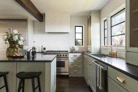 green kitchen cabinets with black countertops, white sone backsplash, white stone range hood, black bar stools