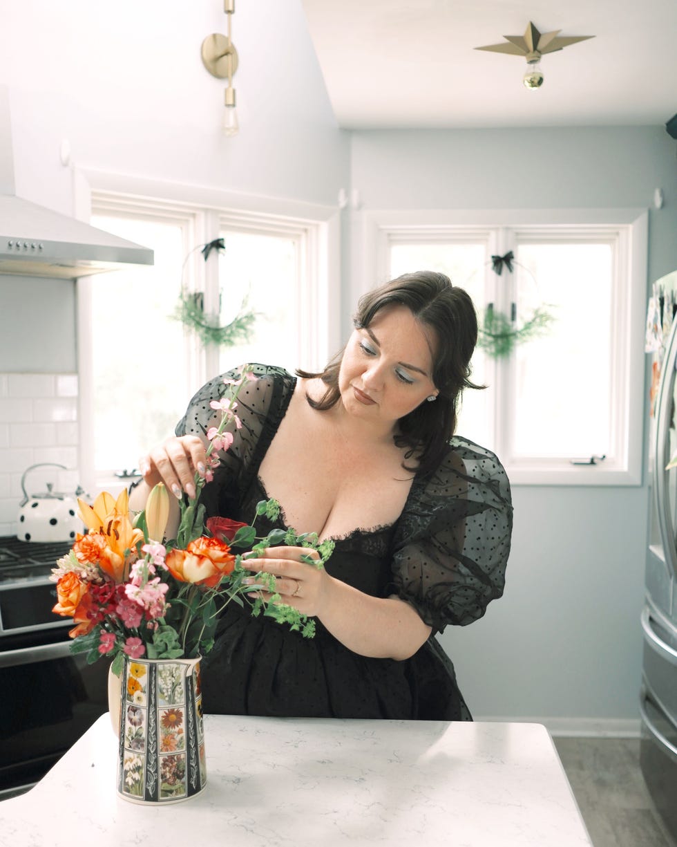 Lynzi Judish artfully arranges a bouquet of flowers while standing in her kitchen wearing a black dress