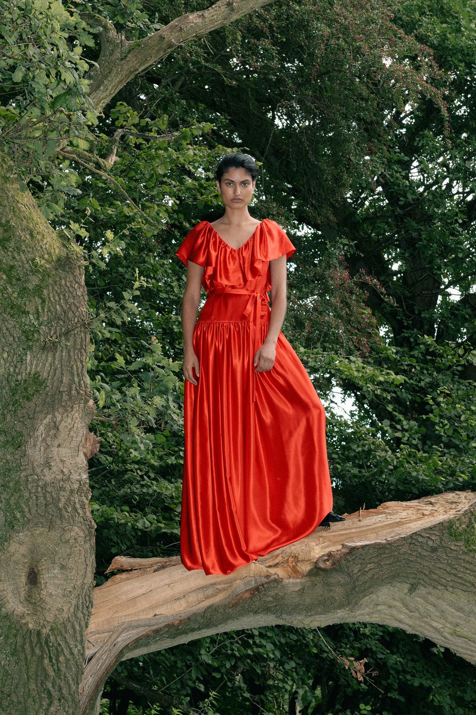 a person in a red dress standing on a tree branch
