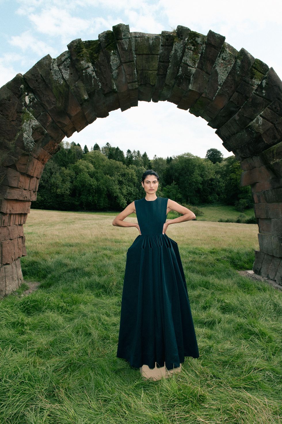 a person in a dress standing in front of a stone arch