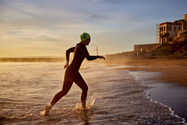 early 50s female triathlete striding out of water at dawn