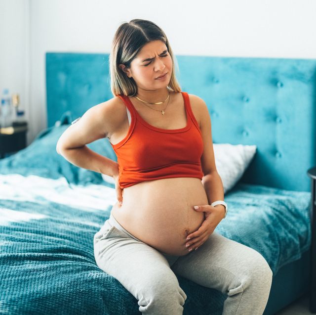 pregnant woman looking slightly in pain while sitting on bed