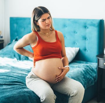 pregnant woman looking slightly in pain while sitting on bed